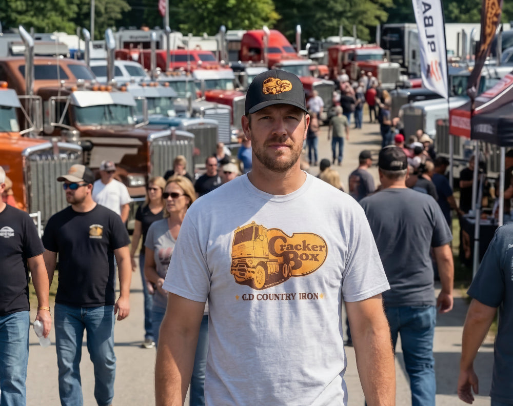 Man wearing a 'Cracker Box' t-shirt at a truck show with various trucks in the background.