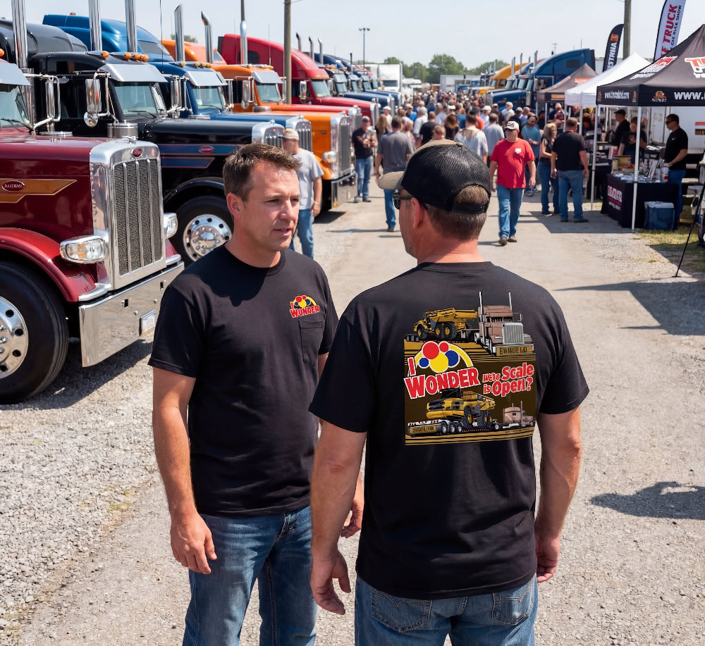 Two men in I Wonder if the Scale is Open t-shirts standing in front of a row of trucks at an outdoor event.