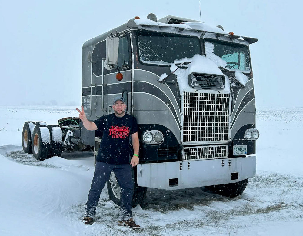 Person standing in front of a truck in a snowy landscape wearing a Trucking Things shirt
